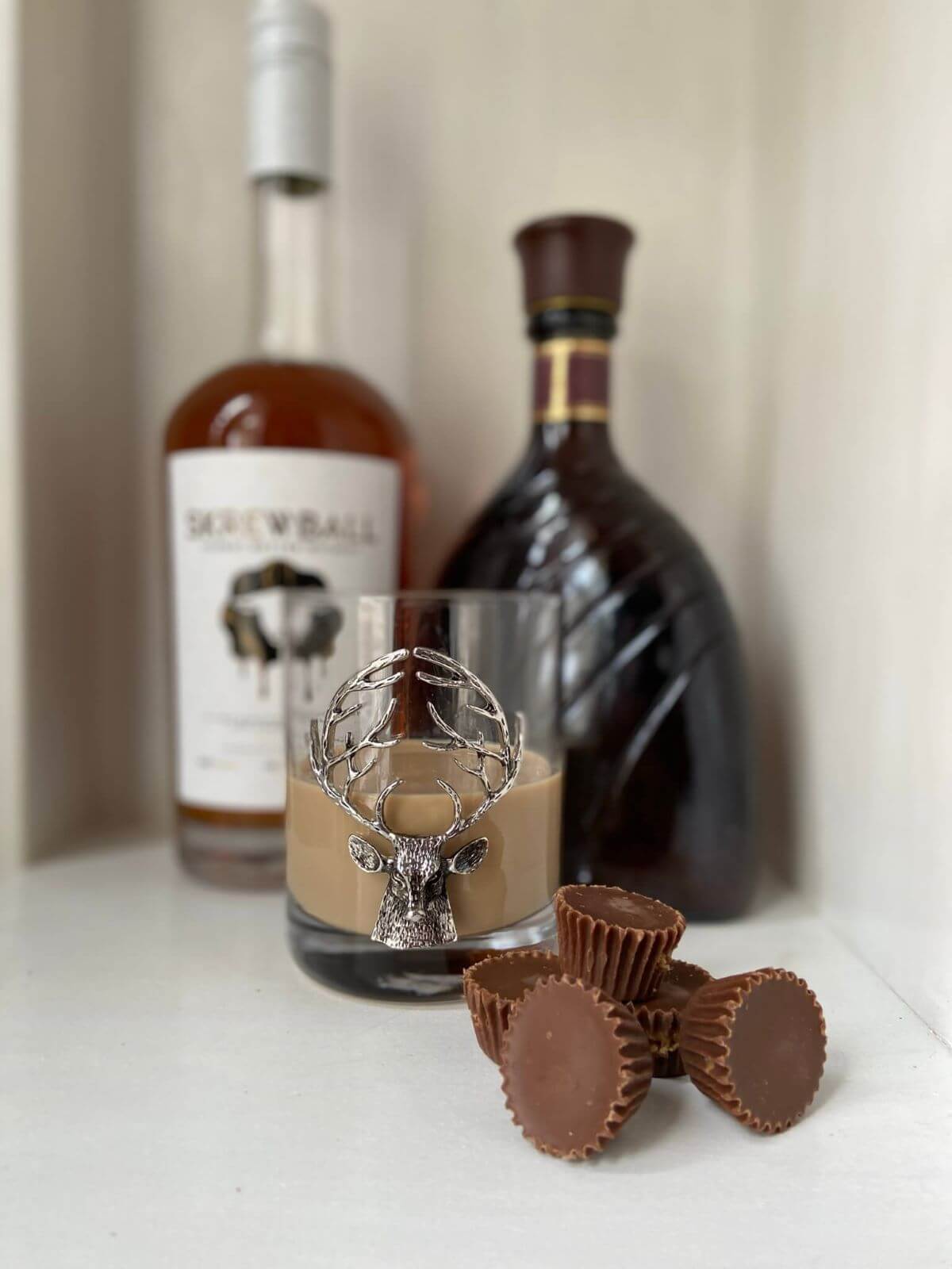 Reeses peanut butter in a cup cocktail with mini reeses pb cups, peanut butter whiskey bottle, and chocolate liqueur bottle 