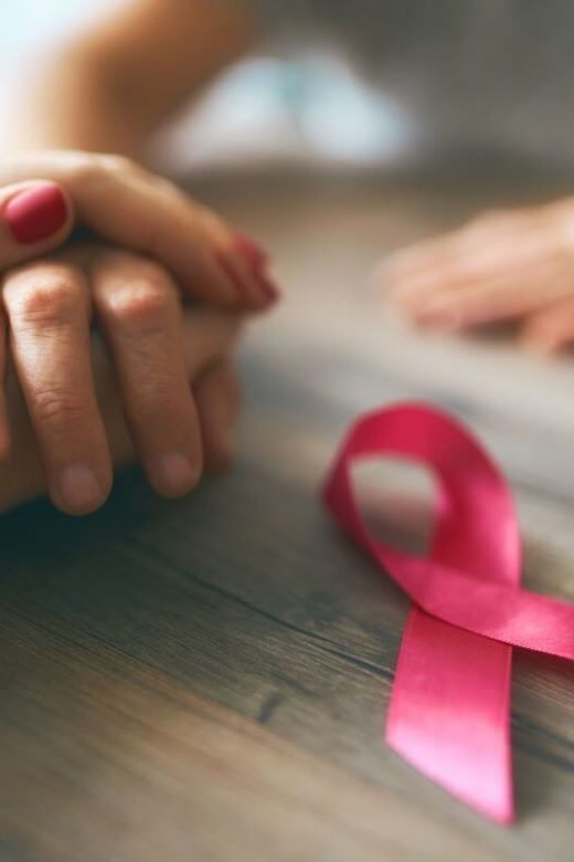 two people holding hands across a table with a pink breast cancer ribbon laying next to their hands