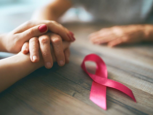 two people holding hands across a table with a pink breast cancer ribbon laying next to their hands