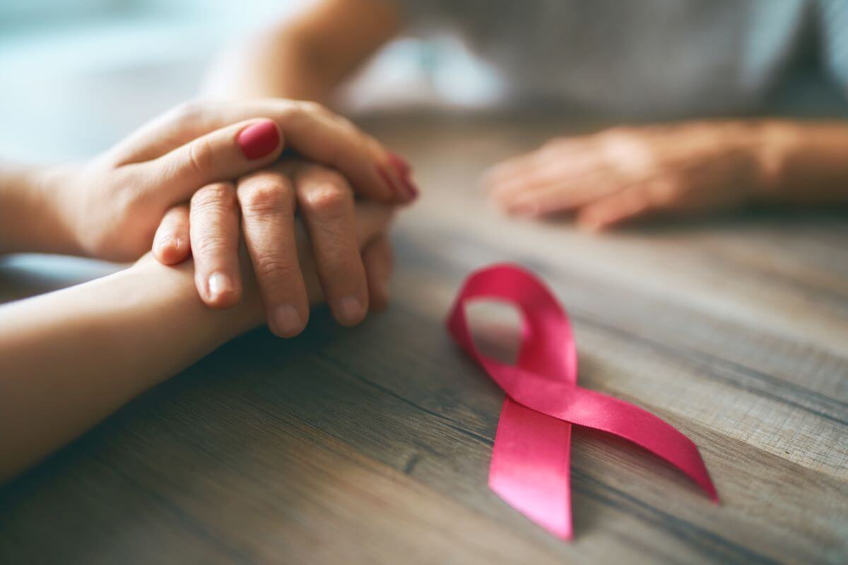 two people holding hands across a table with a pink breast cancer ribbon laying next to their hands