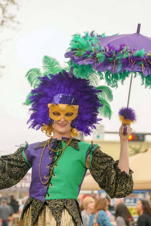 Mardi Gras participant wearing mask, green and purple costume and holding umbrella and beads.