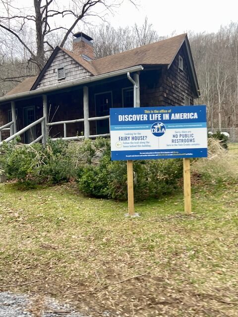 The blue and white sign in front of the Discover Life in America office showing directions to the Fairy House.