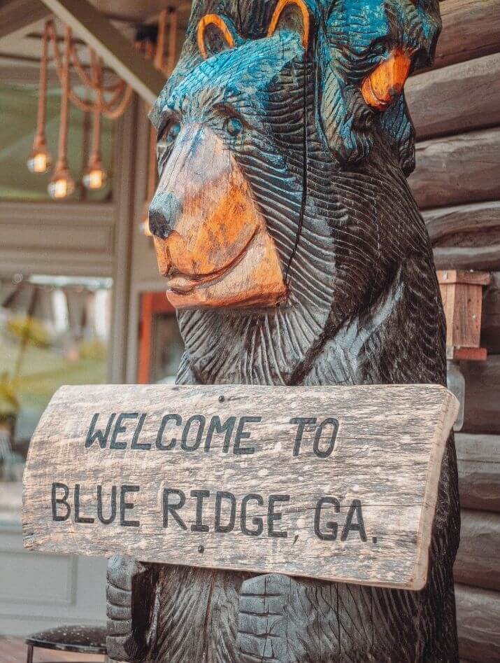 Wooden carved bear holding a sign that says "Welcome to Blue Ridge, GA"